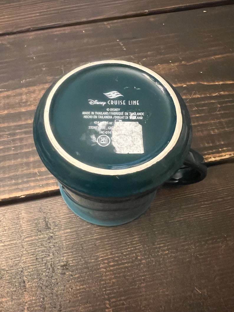 May include: A teal ceramic mug with a white rim, featuring the "Disney Cruise Line" logo and text. The mug is made of stoneware and has a capacity of 16 oz. The mug is teal with a white rim and a black handle.