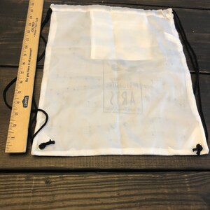 May include: White drawstring bag with black drawstrings. The bag has a small logo that says "Performing Arts" in black text.