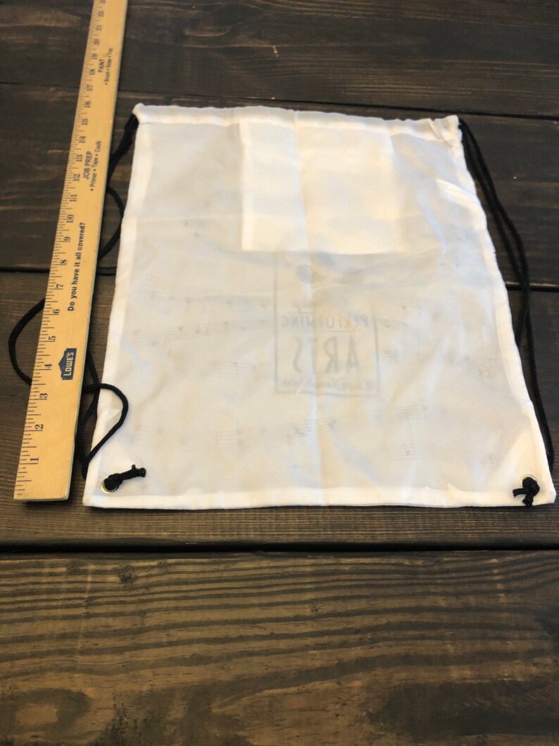 May include: White drawstring bag with black drawstrings. The bag has a small logo that says "Performing Arts" in black text.