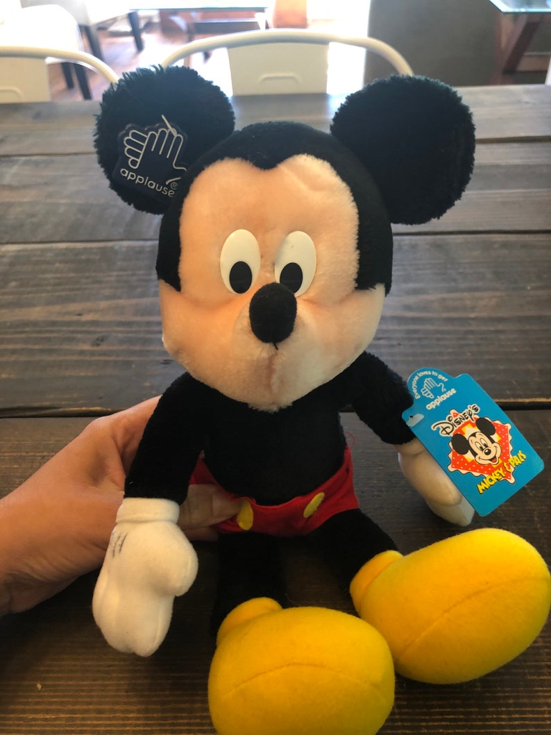 May include: A black and yellow plush Mickey Mouse toy with a red and white shirt and a blue tag that says "Disney's Mickey & Pals".
