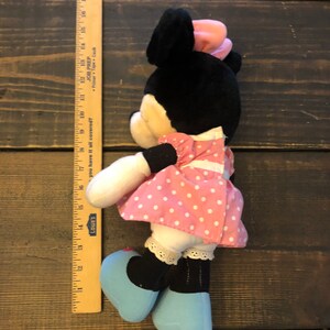May include: A plush toy of Minnie Mouse wearing a pink polka dot dress and blue shoes. She has a pink bow on her head and a black and white face.