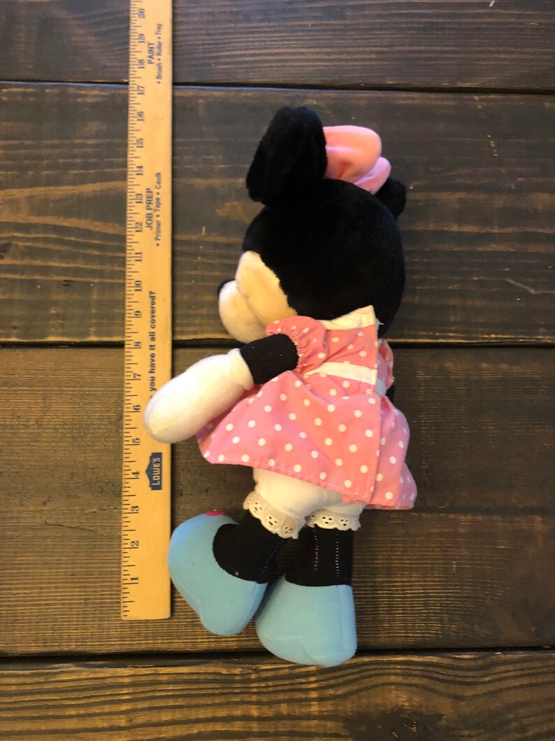May include: A plush toy of Minnie Mouse wearing a pink polka dot dress and blue shoes. She has a pink bow on her head and a black and white face.