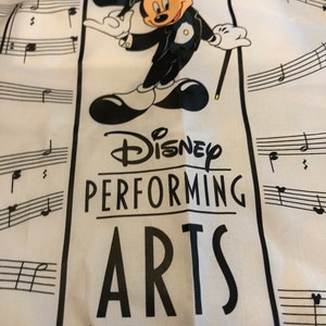May include: A white tote bag with a black and white illustration of Mickey Mouse dressed in a tuxedo. The bag has the text "Disney Performing Arts Walt Disney World." printed on it.