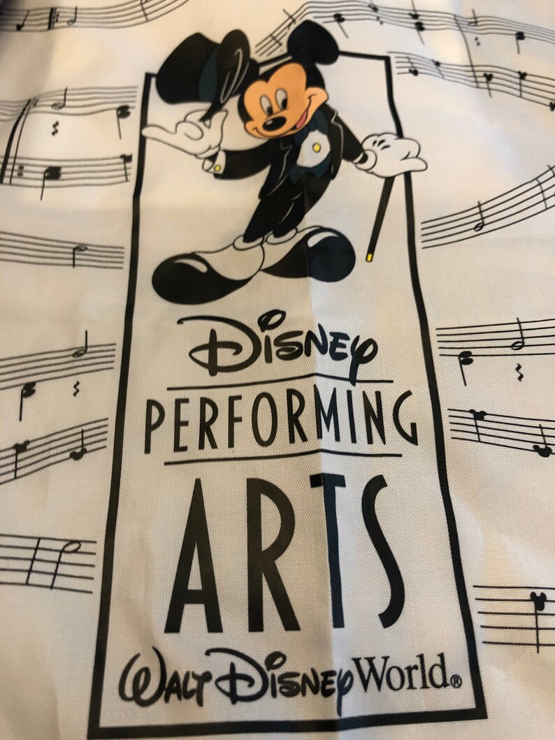 May include: A white tote bag with a black and white illustration of Mickey Mouse dressed in a tuxedo. The bag has the text "Disney Performing Arts Walt Disney World." printed on it.