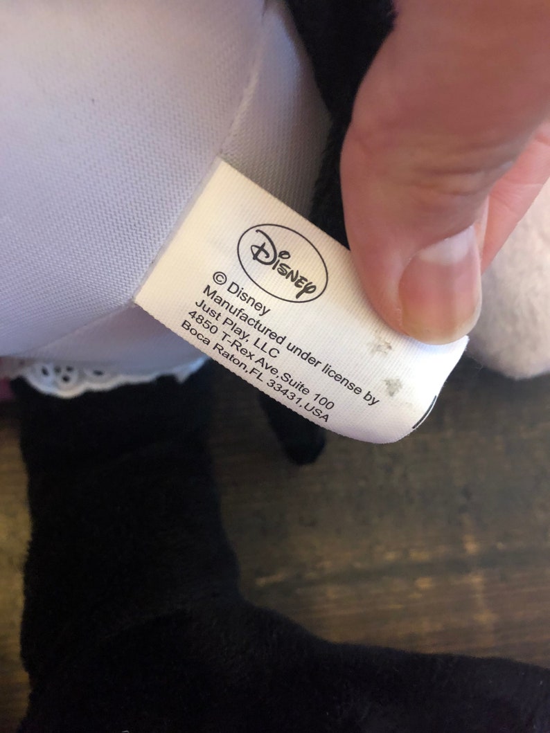 May include: White tag with black text that reads "Disney", "&copy; Disney", "Manufactured under license by Just Play, LLC", "4850 T-Rex Ave, Suite 100", "Boca Raton, FL 33431, USA".