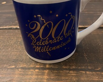 May include: A blue ceramic mug with a white interior and a gold inscription that reads "2000 Celebrate the Millennium".