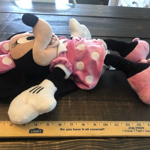 May include: A plush toy of Minnie Mouse lying on its back. Minnie is wearing a pink dress with white polka dots and a pink bow. The toy is approximately 15 inches long.