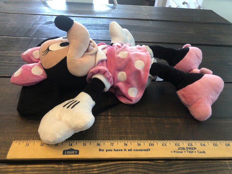 May include: A plush toy of Minnie Mouse lying on its back. Minnie is wearing a pink dress with white polka dots and a pink bow. The toy is approximately 15 inches long.