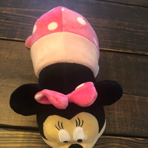 May include: A pink and white polka dot plush toy shaped like Minnie Mouse. The toy has a black nose, large black ears, and a pink bow.