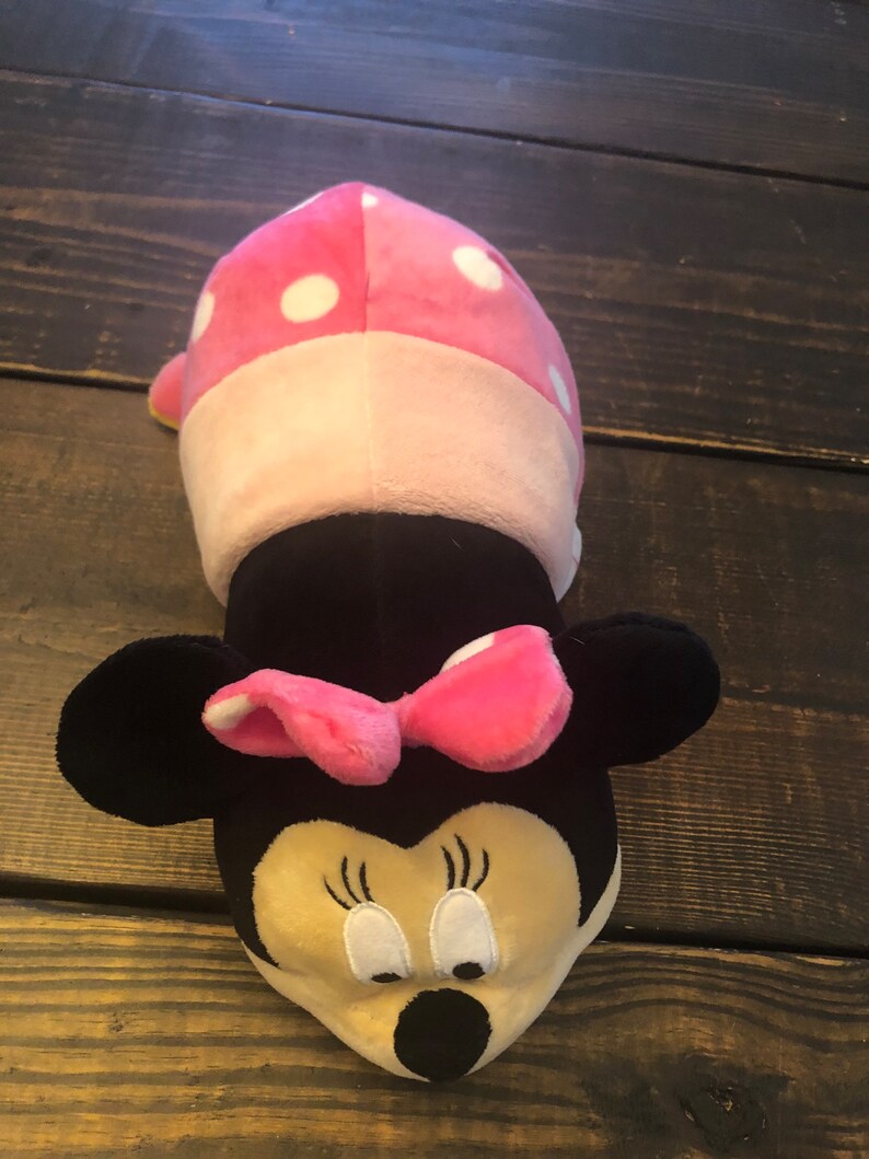May include: A pink and white polka dot plush toy shaped like Minnie Mouse. The toy has a black nose, large black ears, and a pink bow.