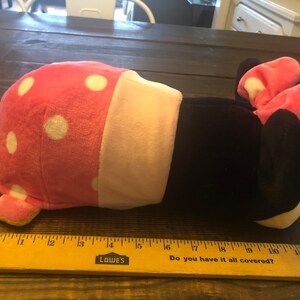 May include: A pink and black plush toy shaped like a cartoon mouse. The mouse is lying on its side with its head resting on the table. The toy has white polka dots on its pink body and a pink bow on its head.