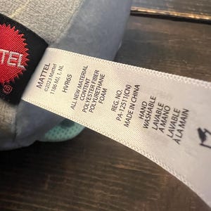 Pode incluir: Uma caneca de cer&acirc;mica branca com uma al&ccedil;a preta e o texto "But First, Coffee" em preto, com uma fonte manuscrita. A caneca est&aacute; sobre uma superf&iacute;cie branca.
