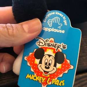 May include: A blue and white tag with the text "Disney's Mickey & Pals" and a cartoon image of Mickey Mouse. The tag also has the text "Everyone loves to get applause" with a hand clapping.