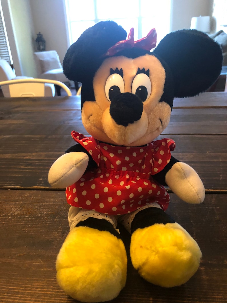 K&ouml;nnte beinhalten: Ein Pl&uuml;schtier von Minnie Mouse, die ein rotes Kleid mit wei&szlig;en Punkten und eine rote Schleife tr&auml;gt. Sie hat schwarze Ohren und eine schwarze Nase. Ihre Augen sind gro&szlig; und schwarz.