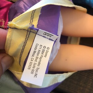 May include: A purple and yellow doll dress with a white label that reads "&copy; Disney &copy;2004 Playmates Toys, INC. 611 Anton Blvd. Suite 600 Costa Mesa, CA 92626" and "LB1813".