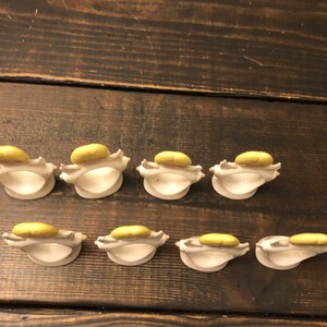 Puede incluir: Ocho anillos de servilleta de cer&aacute;mica con un esmalte amarillo. Cada anillo tiene forma de concha con un dise&ntilde;o en relieve.