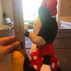 May include: A red and black plush toy of Minnie Mouse, wearing a red dress with white polka dots and a red bow. The toy is approximately 15 inches tall.