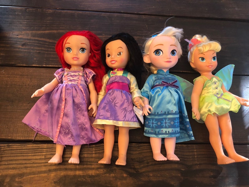 May include: Four Disney princess dolls, including Ariel, Mulan, Elsa, and Tinkerbell. The dolls are wearing their signature dresses and have detailed facial features.