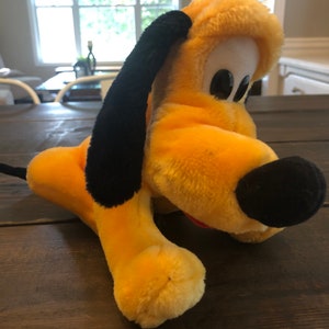 May include: A yellow plush toy dog with black ears and a black nose. The dog is lying on its side with its head turned to the right. The dog is on a wooden surface.