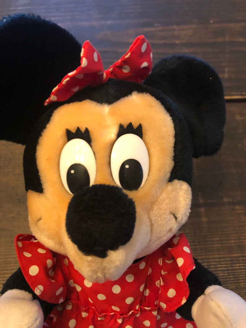 K&ouml;nnte beinhalten: Ein Pl&uuml;schtier von Minnie Mouse, die ein rotes Kleid mit wei&szlig;en Punkten und eine rote Schleife mit wei&szlig;en Punkten tr&auml;gt. Sie hat gro&szlig;e schwarze Augen und eine schwarze Nase.
