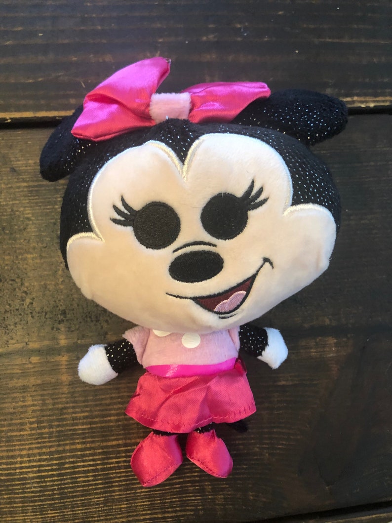 May include: A plush toy of Minnie Mouse wearing a pink dress and a pink bow. She has black eyes, a black nose, and a pink mouth. The toy is about 10 inches tall.