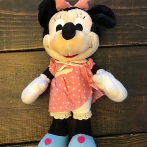 May include: A plush Minnie Mouse doll wearing a pink polka dot dress with a white lace trim and blue shoes with pink hearts.