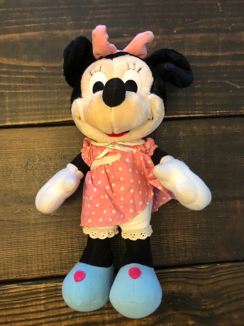 May include: A plush Minnie Mouse doll wearing a pink polka dot dress with a white lace trim and blue shoes with pink hearts.