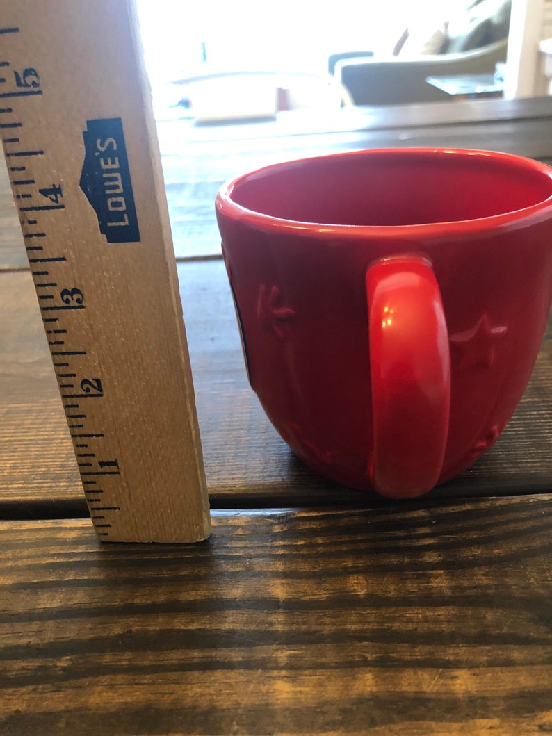 May include: A red ceramic mug with a star design and a handle. The mug is sitting on a wooden surface.