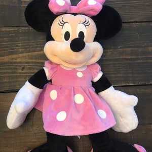 May include: A large pink plush Minnie Mouse toy with white polka dots on her dress and bow. She has black ears and shoes with pink bows.