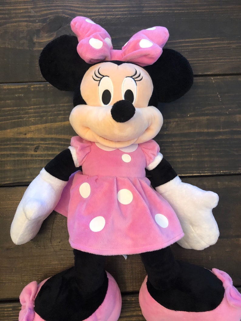 May include: A large pink plush Minnie Mouse toy with white polka dots on her dress and bow. She has black ears and shoes with pink bows.
