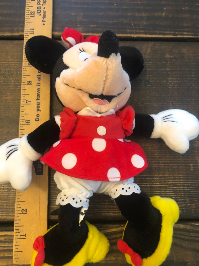 May include: A plush toy of Minnie Mouse wearing a red dress with white polka dots, a black bow, and yellow shoes. The toy is about 8 inches tall and is made of soft, cuddly material.