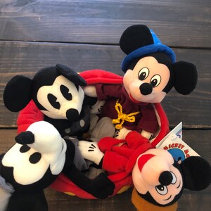 Peut inclure: Quatre peluches Mickey Mouse dans un panier rouge et jaune. Les peluches Mickey Mouse portent des tenues diff&eacute;rentes, dont un chapeau bleu, une robe rouge et un chapeau marron. Le panier a une bordure jaune et un int&eacute;rieur rouge.
