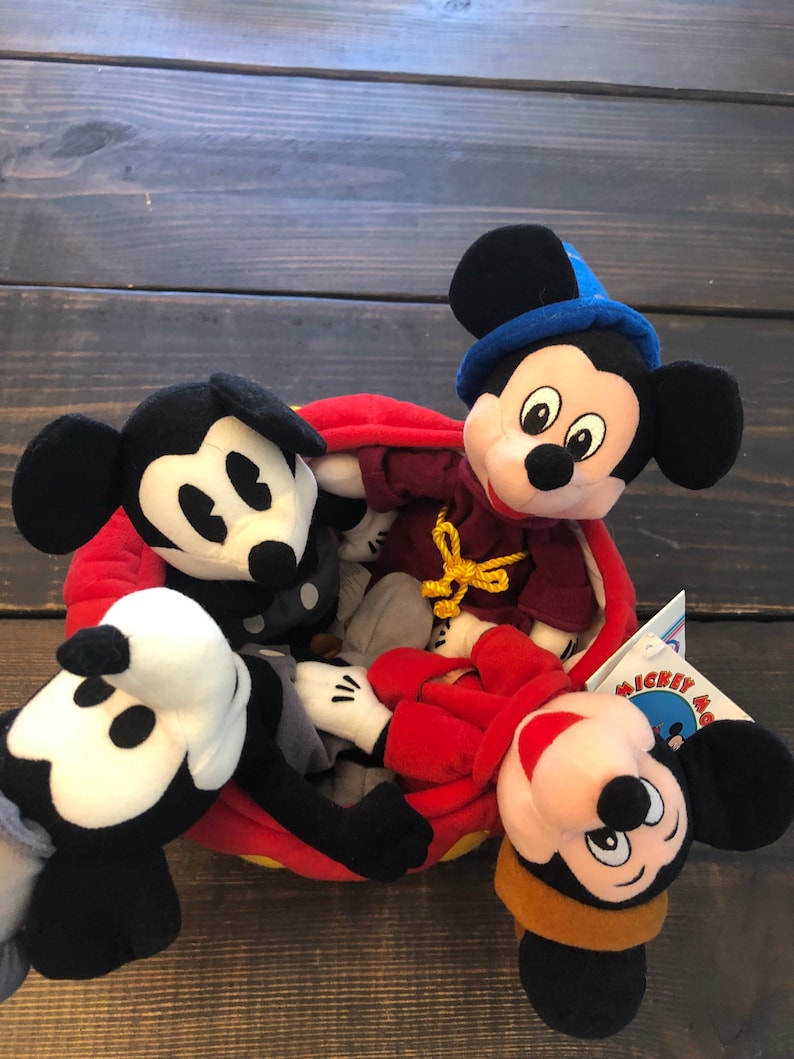 Peut inclure: Quatre peluches Mickey Mouse dans un panier rouge et jaune. Les peluches Mickey Mouse portent des tenues diff&eacute;rentes, dont un chapeau bleu, une robe rouge et un chapeau marron. Le panier a une bordure jaune et un int&eacute;rieur rouge.