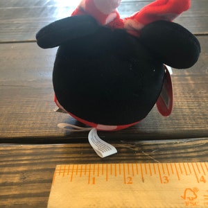 Op de afbeelding: Een pluche speelgoed in de vorm van Mickey Mouse met een rode strik met witte stippen. Het speelgoed is ongeveer 7,5 cm hoog.