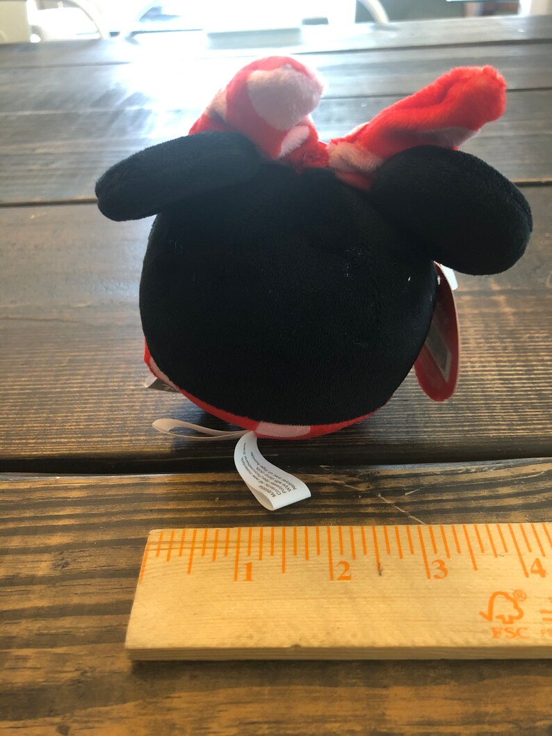 Op de afbeelding: Een pluche speelgoed in de vorm van Mickey Mouse met een rode strik met witte stippen. Het speelgoed is ongeveer 7,5 cm hoog.
