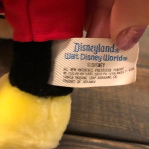 May include: A white tag with blue text that reads "Disneyland Walt Disney World" and "DISNEY" with additional information about the product's materials and origin.