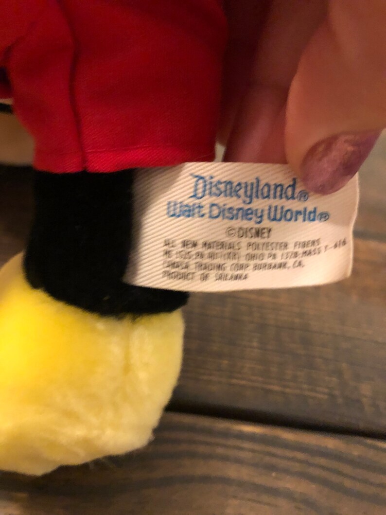 May include: A white tag with blue text that reads "Disneyland Walt Disney World" and "DISNEY" with additional information about the product's materials and origin.