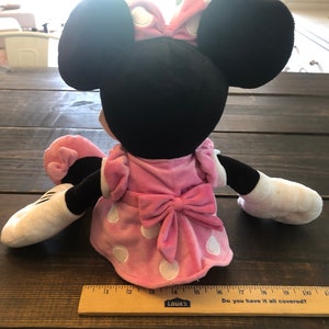 May include: A plush Minnie Mouse toy wearing a pink dress with white polka dots and a pink bow. The toy has black ears and a white face.