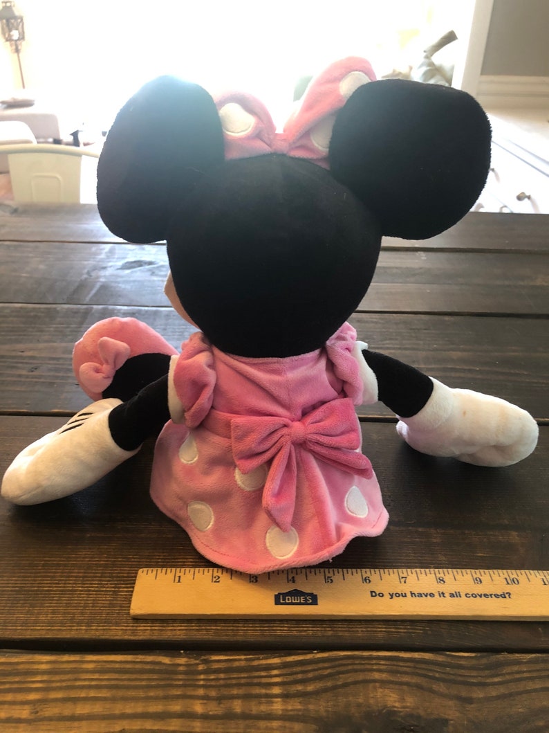 May include: A plush Minnie Mouse toy wearing a pink dress with white polka dots and a pink bow. The toy has black ears and a white face.