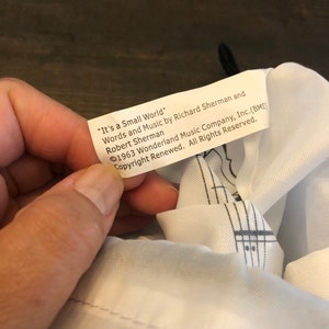 May include: A white fabric bag with a black and white musical note design. The bag has a label that reads "It's a Small World" Words and Music by Richard Sherman and Robert Sherman &copy;1963 Wonderland Music Company, Inc. (BMI) Copyright Renewed. All Rights Reserved.