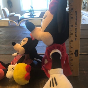 May include: Two plush Mickey Mouse toys, one red and white with black polka dots and the other black and white with red polka dots. The larger toy is holding a yellow plush ball with a red bow.