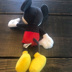 Puede incluir: Un juguete de peluche Mickey Mouse negro y rojo con zapatos amarillos. El juguete mide aproximadamente 38 cm de alto.