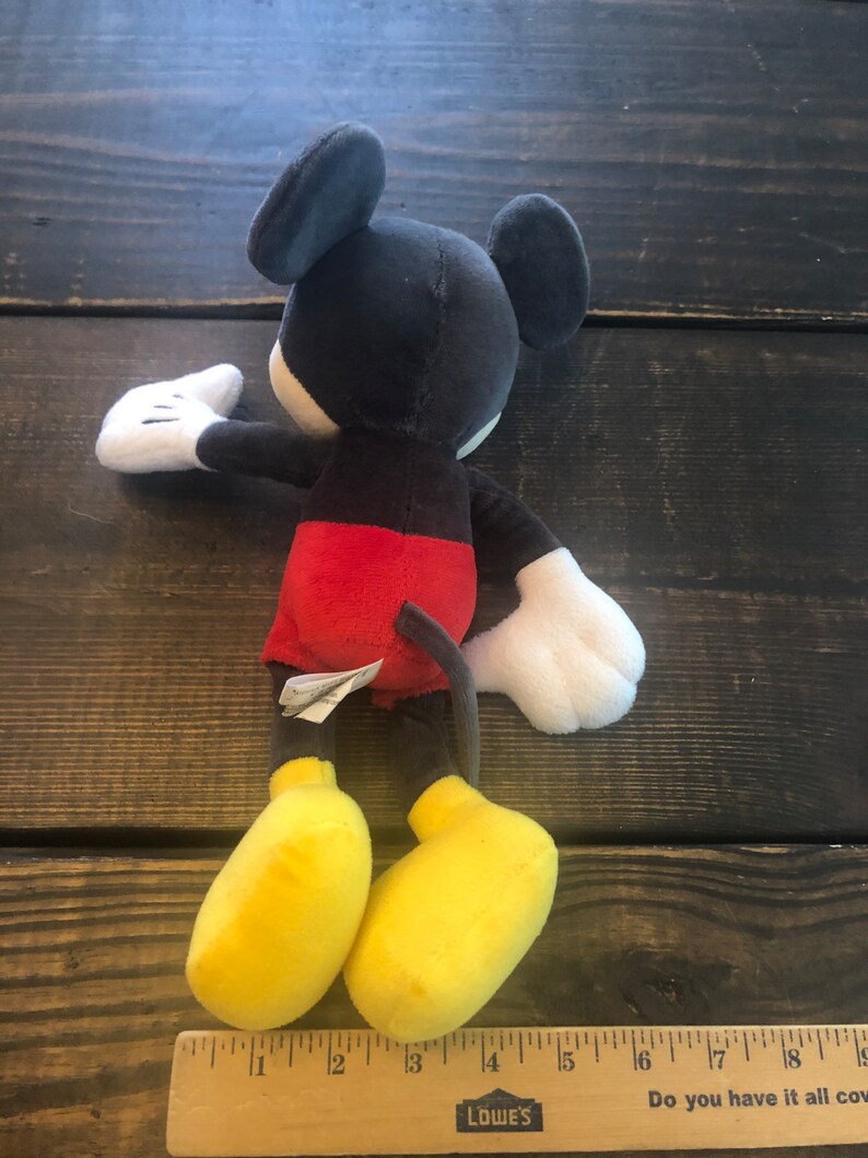 Puede incluir: Un juguete de peluche Mickey Mouse negro y rojo con zapatos amarillos. El juguete mide aproximadamente 38 cm de alto.