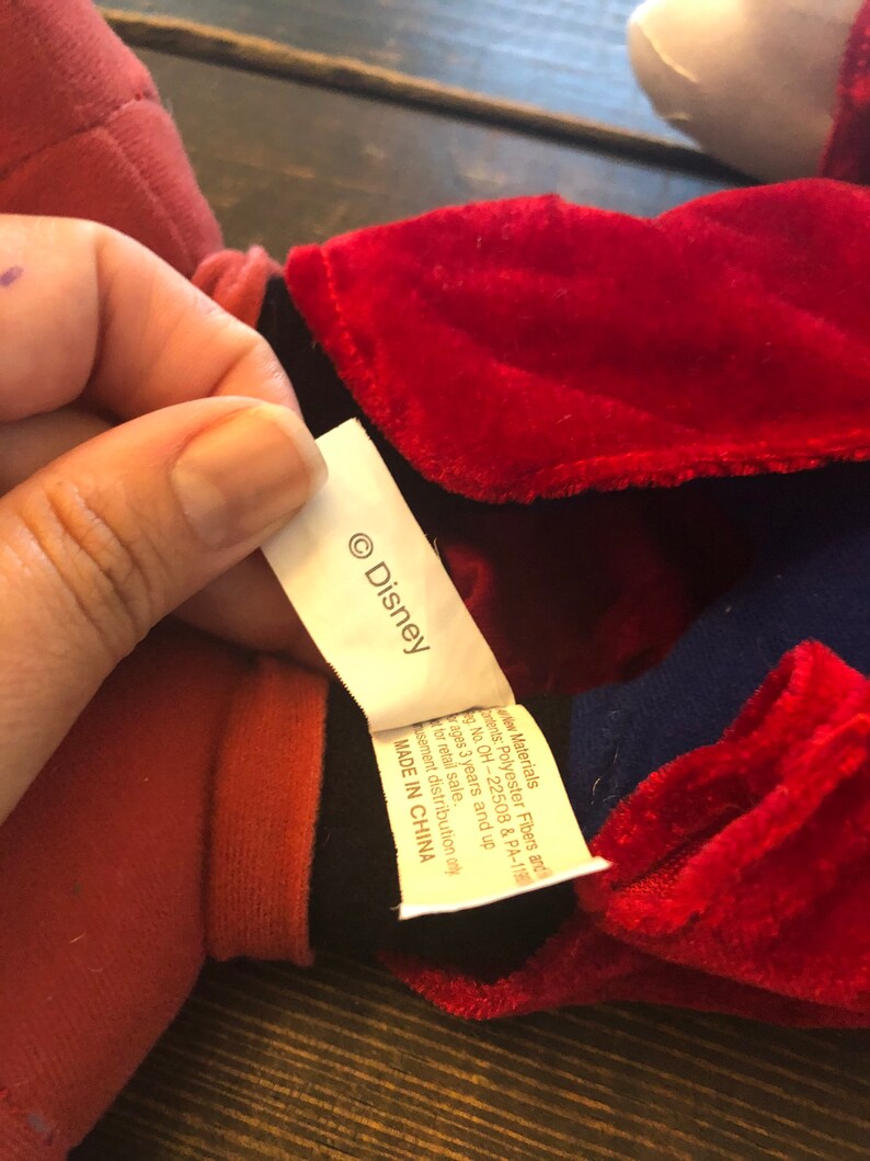 May include: A red and blue plush toy with a black collar and a white tag that says "&copy; Disney". The tag also says "New Materials: Polyester Fibers and  Fill. Reg. No. OH-22508 & PA-1190. Ages 3 years and up. For retail sale.  Amusement distribution only. MADE IN CHINA."