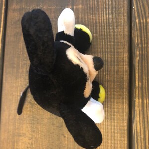 May include: Black and white plush Mickey Mouse toy with yellow accents. The toy is lying on its side with its head tilted to the right.