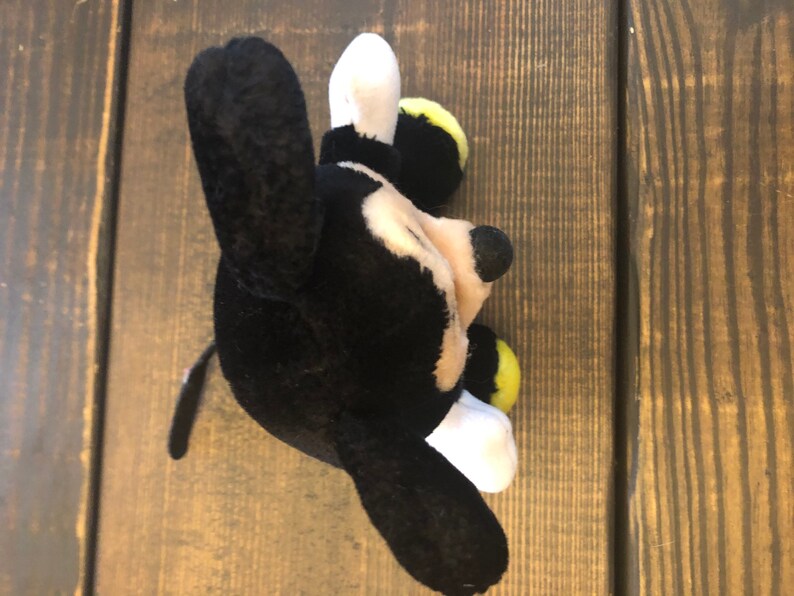 May include: Black and white plush Mickey Mouse toy with yellow accents. The toy is lying on its side with its head tilted to the right.
