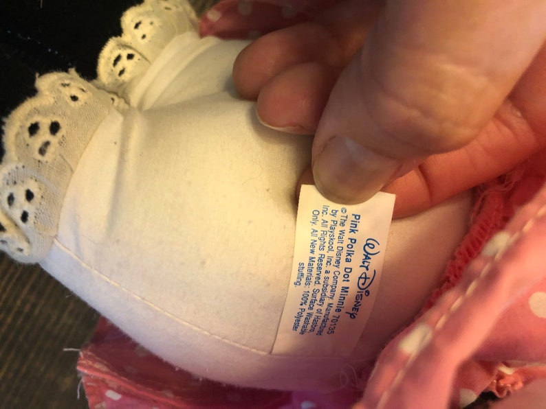 May include: Pink polka dot Minnie Mouse plush toy with a white lace trim and a white tag that reads "WALT DISNEY Pink Polka Dot Minnie 70135 The Walt Disney Company. Manufacture by Playskool, Inc. a subsidiary of Has Inc. All Rights Reserved. Surface Washable Only. All New Materials: 100% Polyester stuffing."