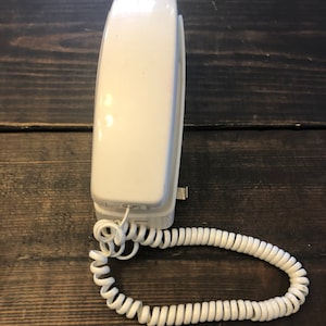May include: A white rotary phone with a coiled cord. The phone has a simple design with no visible buttons or features.
