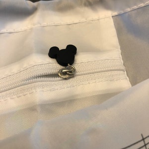 May include: A white drawstring bag with a black Mickey Mouse head zipper pull. The bag has a musical note pattern on the bottom.