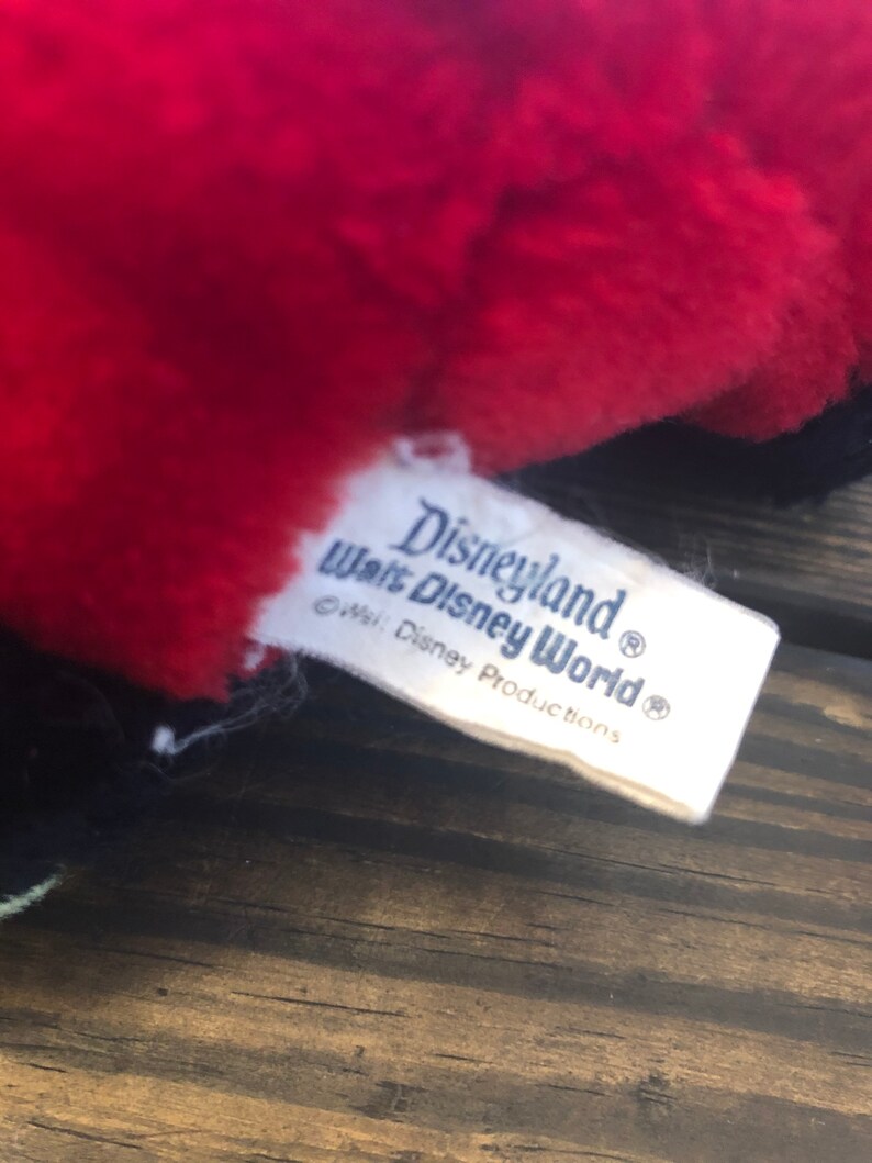 May include: White tag with blue text that reads "Disneyland Walt Disney World" with a copyright symbol and the text "c Walt Disney Productions" with a registered trademark symbol.